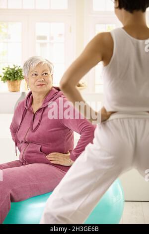 Donna anziana che guarda personal trainer Foto Stock