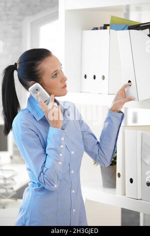 Ragazza in ufficio che prende la cartella mentre sul telefono Foto Stock