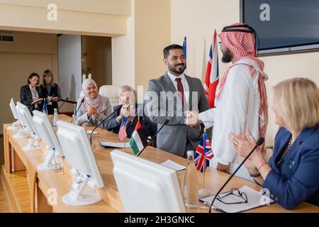 Sorridente politico di razza mista in tuta facendo stretta di mano con i rappresentanti arabi in thibe alla conferenza Foto Stock