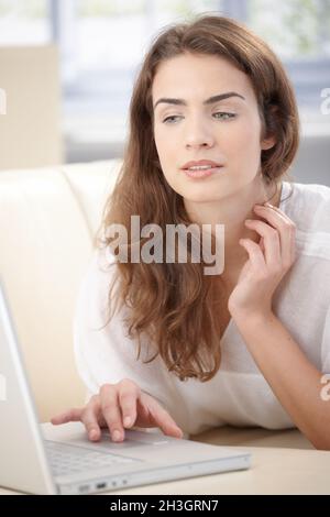 Giovane donna che usa un computer portatile adagiato su un divano Foto Stock