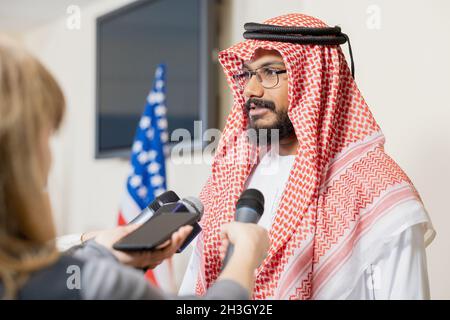 Politico medio-orientale in abiti nazionali rispondendo alle domande dei media da giornalisti con microfoni dopo conferenza Foto Stock