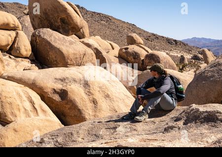 Donna Hiker siede e guarda fuori in lontananza nella natura selvaggia di Joshua Tree Foto Stock