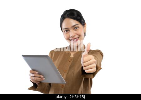 Donna indonesiana in uniforme di funzionario con i pollici in su mentre usando la compressa Foto Stock