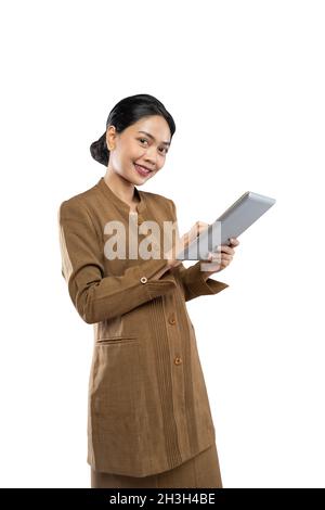 Donna indonesiana in uniforme di funzionario con i pollici in su mentre usando la compressa Foto Stock