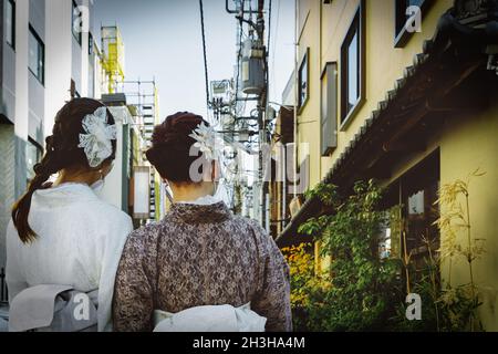 Due donne, vestite in kimono formale, guardano giù per una strada a Tokyo, Giappone. Foto Stock