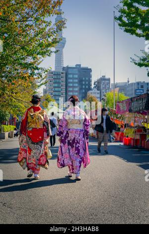 Due donne, vestite in kimono formale, camminano attraverso una zona centrale di Tokyo, Giappone. Foto Stock