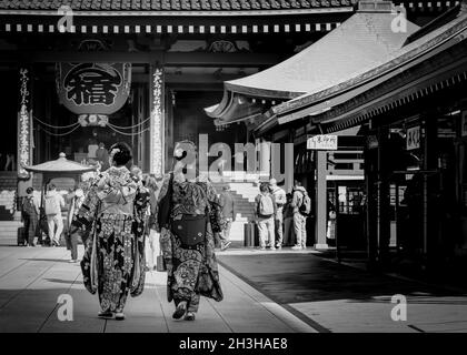 Due donne, vestite in kimono formale, passano vicino ad un tempio di Tokyo, Giappone. Foto Stock