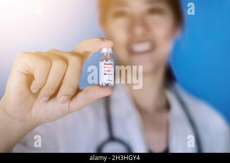 Vaccino MMR o morbillo, parotite e rosolia. Medico donna che indossa un cappotto bianco con uno stetoscopio intorno alla spalla che tiene una fiala di vetro di M-M-R va Foto Stock