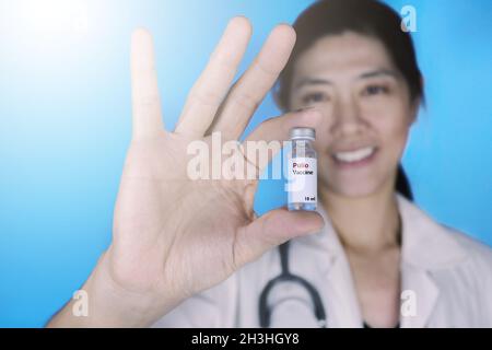 Vaccino antipolio. Medico donna che indossa un cappotto bianco con uno stetoscopio intorno alla spalla che tiene una fiala di vetro di vaccino Polio, sorridente. Assistenza sanitaria e Foto Stock