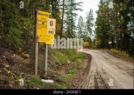 Foto di un cartello stradale disattivato e altri cartelli gialli di guida accanto a una strada montana fangosa e rurale che è stato probabilmente utilizzato per i veicoli di legno da disboscamento. Foto Stock