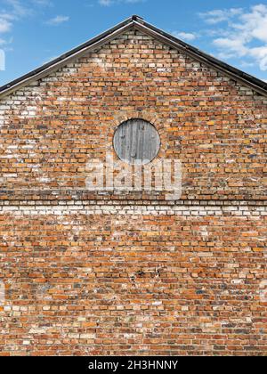 muro a timpano in mattoni rossi con finestra a bordo. vecchio edificio esterno. Foto Stock