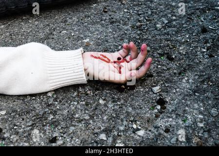 la mano di un uomo è coperta di sangue giacente sull'asfalto della strada. Foto Stock