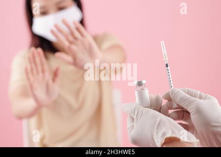 Medico che offre il flaconcino e la siringa per la giovane paziente spaventato in maschera medica Foto Stock