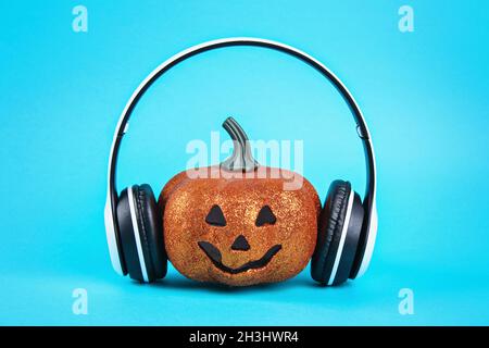 Zucca arancione con cuffie wireless bianche su sfondo blu. Halloween concetto e audio. Foto Stock