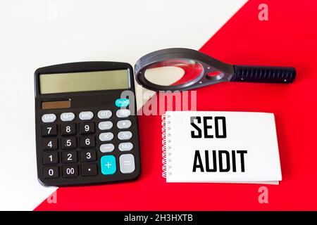 Testo scritto su blocco note, SEO audit report. La calcolatrice e la lente di ingrandimento si trovano su uno sfondo rosso e bianco. Sito web di analisi concettuale Foto Stock