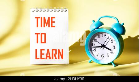 Su uno sfondo chiaro di un notebook, il testo TIME TO LEARN (ORA DI APPRENDIMENTO) viene scritto accanto a una sveglia Foto Stock
