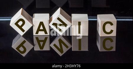 PAROLA DI PANICO fatta da lettere quadrate di legno su sfondo nero lucido. Riflessione speculare. Foto Stock