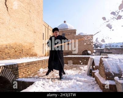 Un assistente libera la neve dal sentiero della necropoli di Shahi-Zinda a Samarcanda, Uzbekistan Foto Stock