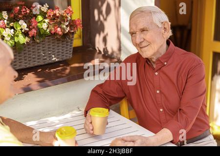 Un gentiluomo anziano allegro trascorre del tempo con la moglie amata in un caffè di strada Foto Stock