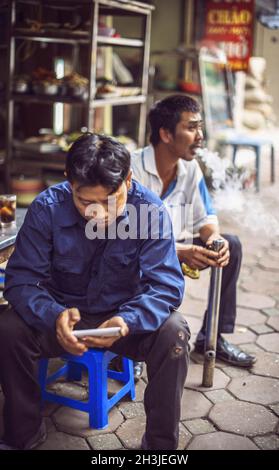 HANOI, VIETNAM - Aprile 8, 2015: Uomini non identificati di fumare il tipico vietnamita tubazione di tabacco in strada, l'8 aprile 2015, in Foto Stock