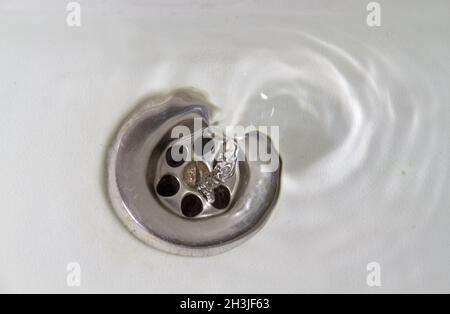 Acqua che scorre via in un lavandino di pietra bianca Foto Stock