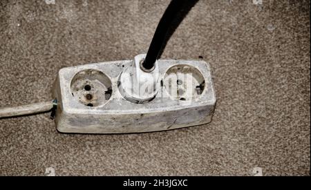 Presa o prese triple già utilizzate e vecchie su moquette con una spina elettrica bianca e un cavo nero. La traduzione di 'TSE' è 'turco standard inst Foto Stock