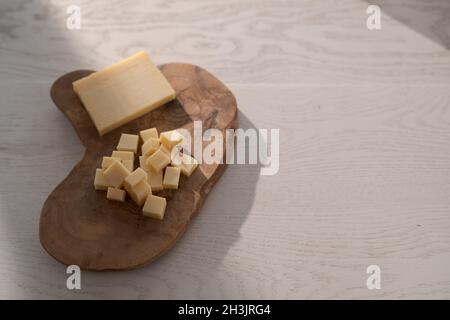 Piccolo blocco di formaggio stagionato affettato in piccoli pezzi su tavola di legno, poco profondo fuoco Foto Stock