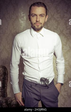 Uomo attraente ed elegante con una pistola nei suoi pantaloni che posano su sfondo vintage Foto Stock