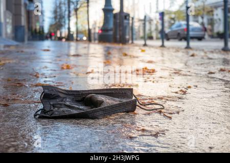 Vecchia maschera usa e getta caduta sul marciapiede in città. Sfondo urbano autunnale Foto Stock