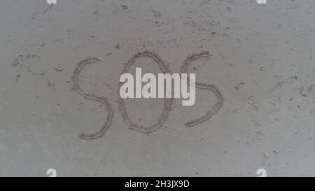 Foto dall'alto di SOS scritto in sabbia sulla spiaggia tropicale Foto Stock