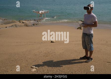 Uomo con telecamera drone e occhiali per realtà virtuale che scattano foto e video sulla spiaggia Foto Stock