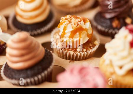 Un sacco di piccoli cupcake colorati con salsa al caramello e altri condimenti Foto Stock