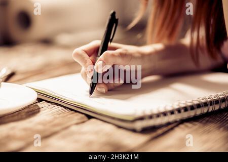 Vista ravvicinata della scrittura a mano del woman con penna su un notebook su un tavolo di legno. Foto Stock