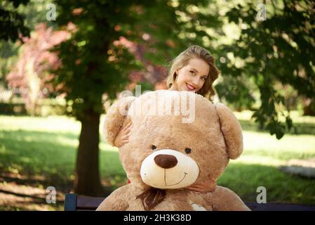 Un enorme orsacchiotto e una giovane sorridente nel parco. Foto Stock