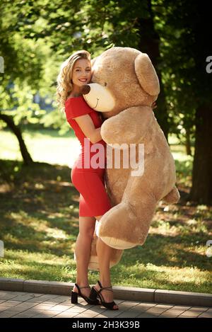 La giovane donna abbraccia un enorme orsacchiotto nel parco. Foto Stock