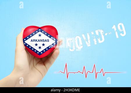 Una ragazza sta tenendo un giocattolo a forma di cuore con la bandiera dello Stato dell'Arkansas, un concetto di assistenza sanitaria durante la pandemia di coronavirus covid-19 Foto Stock