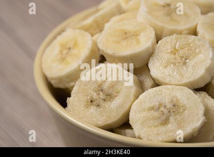 Banana a fette in ciotola di ceramica su sfondo di legno. Primo piano. Foto Stock