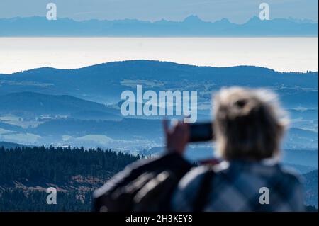 Bayerisch Eisenstein, Germania. 29 ottobre 2021. Una donna scatta una foto dal Großer Arber, alto 1456 metri, nella foresta bavarese, attraverso la foresta bavarese, alle Alpi sullo sfondo, a circa 200 chilometri di distanza. Credit: Armin Weigel/dpa/Alamy Live News Foto Stock