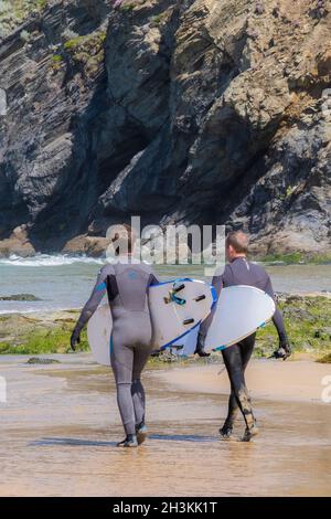 Mawgan Porth Beach in Cornovaglia nel Regno Unito; Surfers che portano le loro tavole da surf che camminano verso il mare in una vacanza di staycation della Cornovaglia. Foto Stock