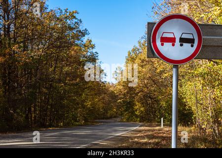 Nessun segnale di sorpasso sullo sfondo di una strada di campagna e di una foresta autunnale. Il concetto di sicurezza stradale Foto Stock