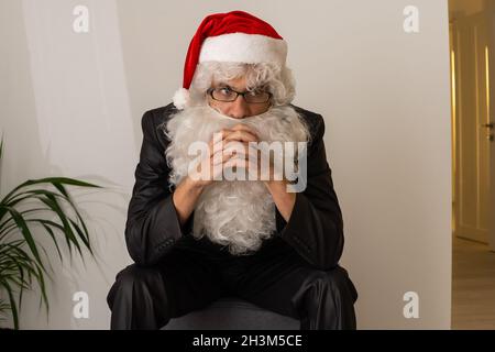 Babbo Natale seduto sulla poltrona e in attesa di Natale, sta appoggiando la testa sulle mani Foto Stock