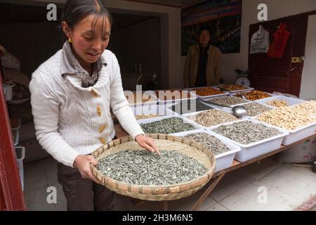 Donna tibetana / donne etniche del Tibet, residente o locale alla città cinese murata antica (antica città murata) di Songpan nel nord Sichuan, Cina. Sta vendendo semi di semi / girasole al suo negozio di tipo di cibo intero nella città. (125) Foto Stock