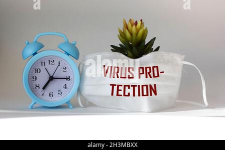 Testo PROTEZIONE VIRUS su maschera medica e sfondo chiaro. Cactus e orologio. Concetto medico. Foto Stock