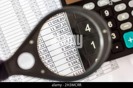 La lente di ingrandimento e la calcolatrice si trovano su un documento con numeri Foto Stock