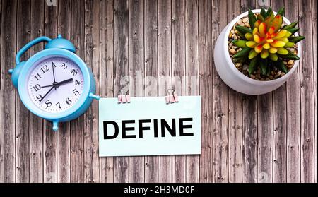 Definire la parola sull'adesivo e sullo sfondo in legno. Vicino ad una sveglia e un fiore di cactus Foto Stock