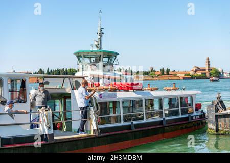 Stazione dei traghetti dell'isola di Murano chiamata Punta Faro con un gruppo di persone, la laguna di Venezia. Sullo sfondo l'isola di San Michele. Veneto, Italia. Foto Stock