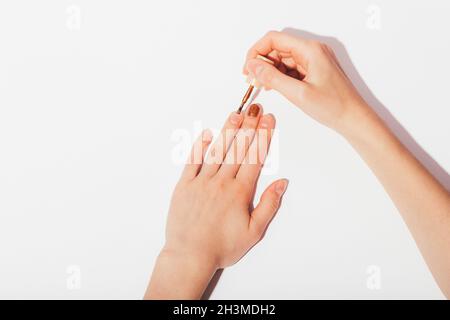 Mani femminili che fanno manicure con lucido marrone unghie lucido su sfondo bianco, primo piano Foto Stock