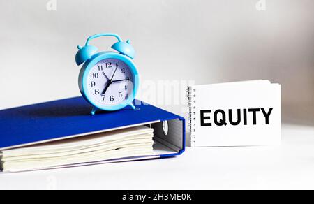 La parola EQUITY è scritta su un blocco note. Cartella documenti e sveglia su sfondo bianco Foto Stock