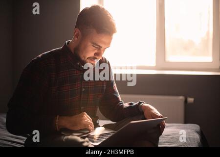 Uomo felice che usa un computer portatile seduto sul letto di casa Foto Stock