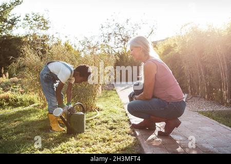 Donna anziana accovacciata mentre guarda il ragazzo con annaffiatura può Foto Stock